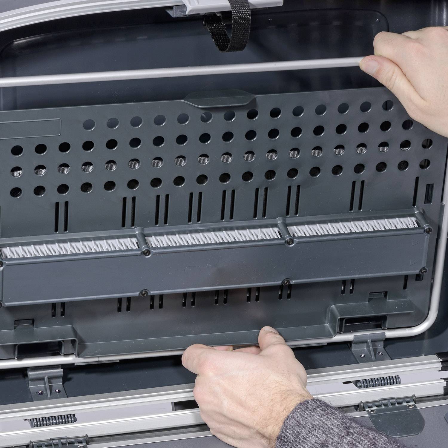 A person is repairing the back panel of a dishwasher. Hands are reaching for screw holes on a metal plate inside the appliance.