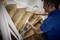 A man in a blue shirt is measuring a staircase with a silver tool. The wooden steps are partially worn and unpainted.