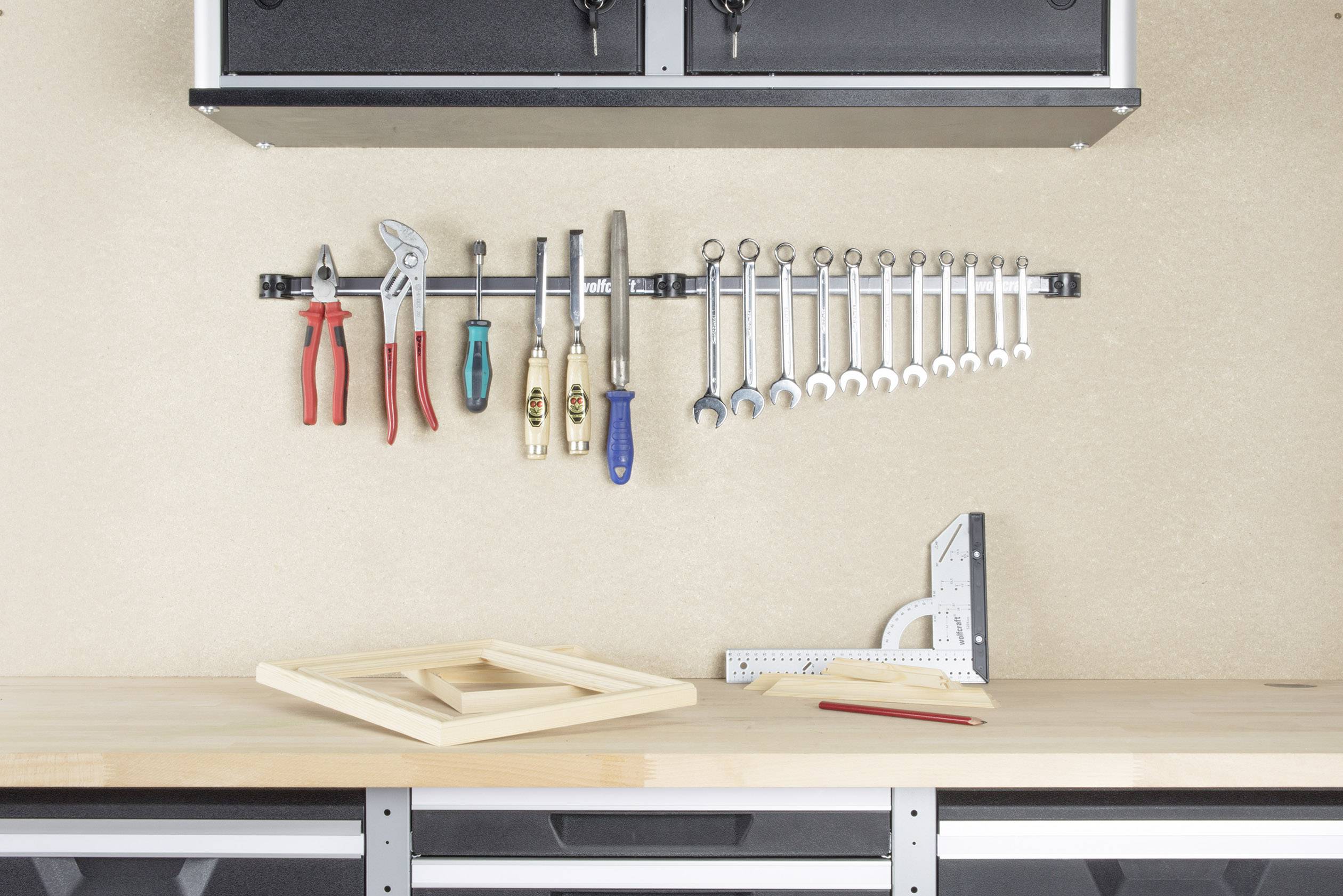 A workbench with a tool set: pliers, spanners and hammers hang on the wall. An angle gauge, a pencil and a wooden frame lie on the work surface.