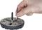 A hand adjusts a screw on a round metal object with multiple slots.