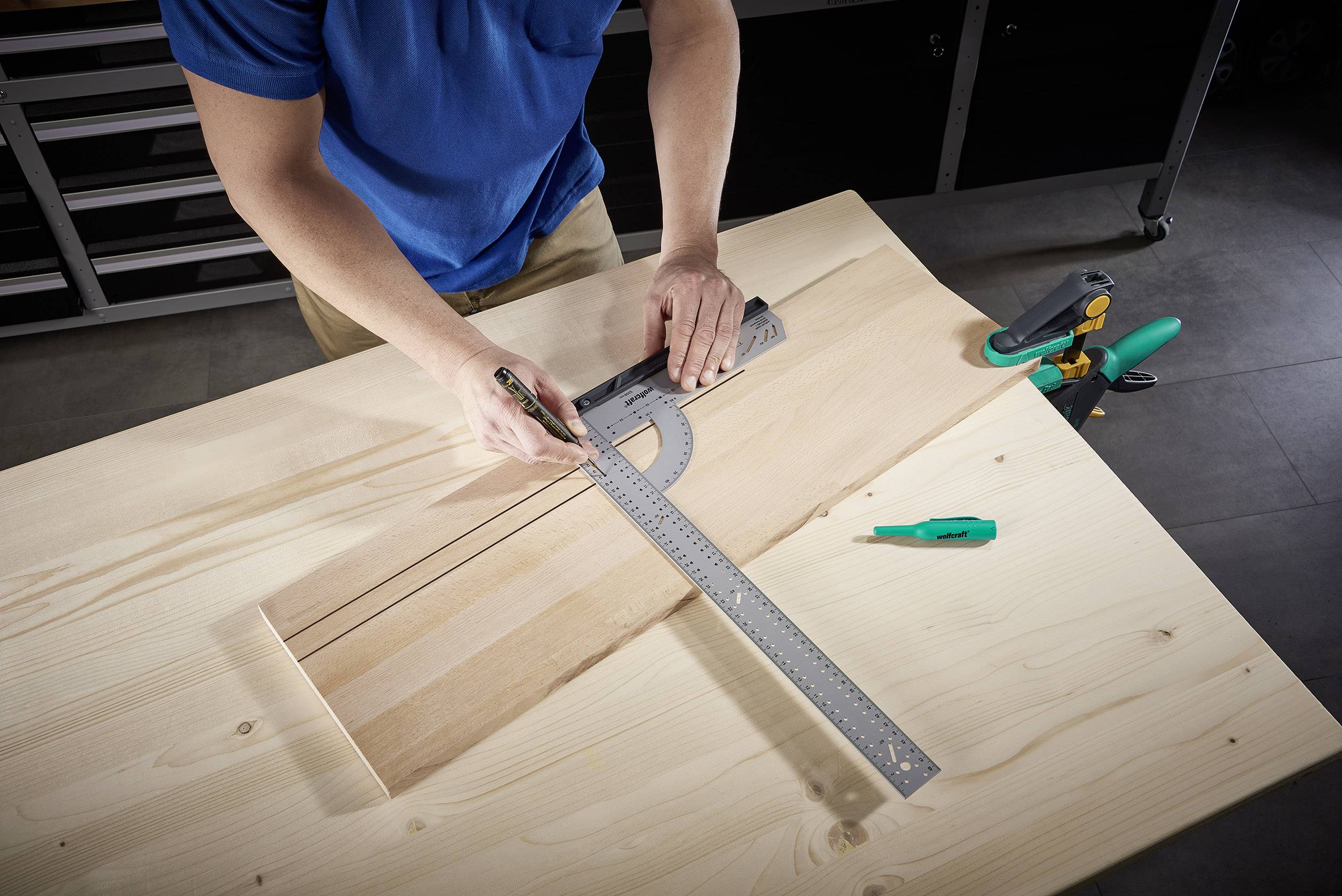 A person is measuring and drawing lines on a wooden board with an angle measurer and ruler in a workshop.