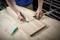 A person measures with a tape measure and marks a wooden board. The scene depicts precision in woodworking.