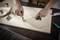 A person is drawing a circle on a wooden board using a measuring tape and a pen. Rolls can be seen in the background.