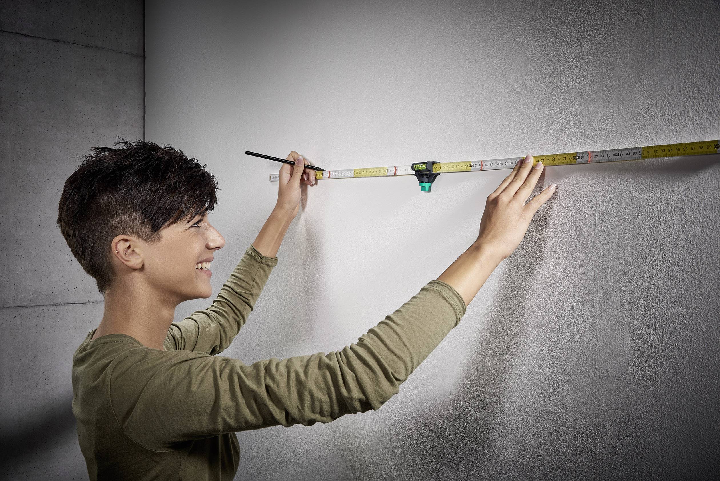A person is measuring a wall with a tape measure. They are holding the tape measure and marking the measurement with a pencil.