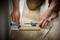 A person is measuring a wooden board with an angle measure for precise cutting, with a pencil lying beside it on the floor.