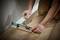 A person is measuring the width of a gap to the wall using a tool to cut laminate flooring precisely.