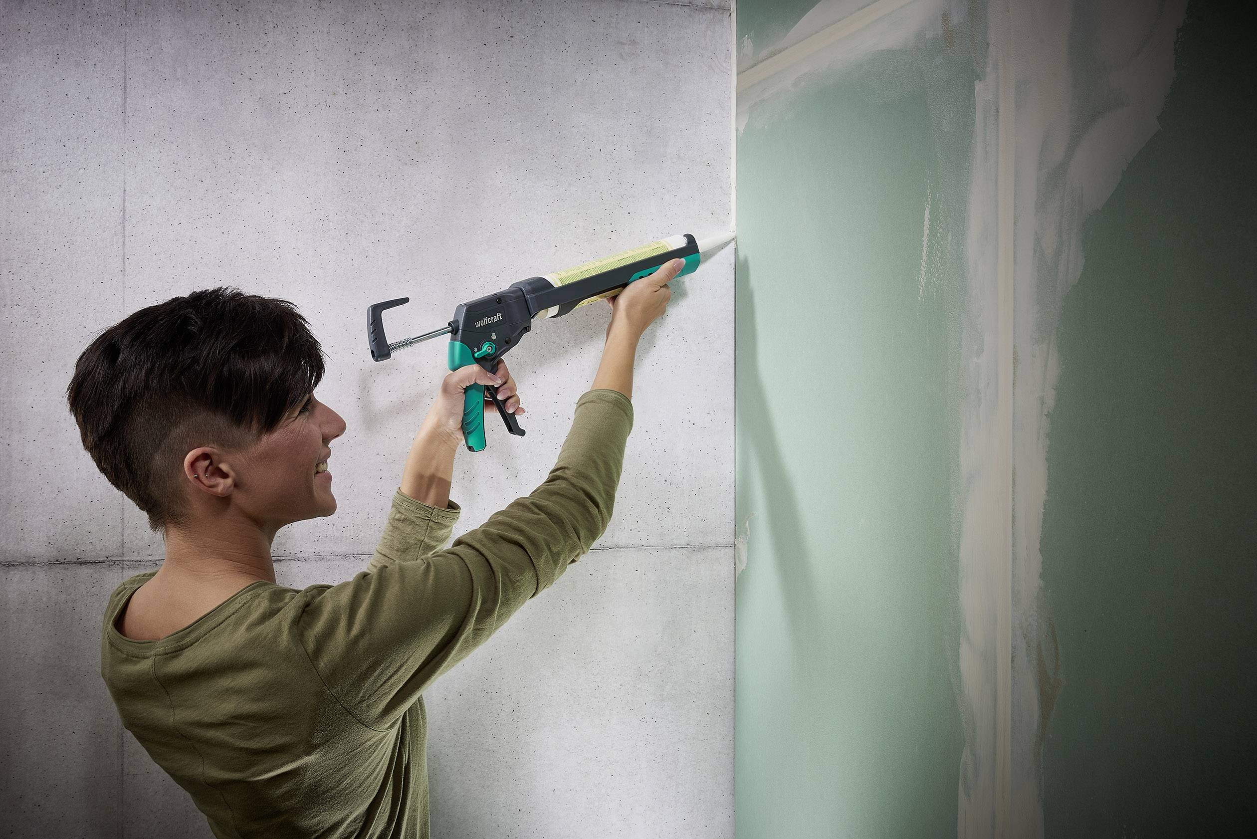 A person is sealing a gap between a plasterboard and concrete wall using a caulking gun.