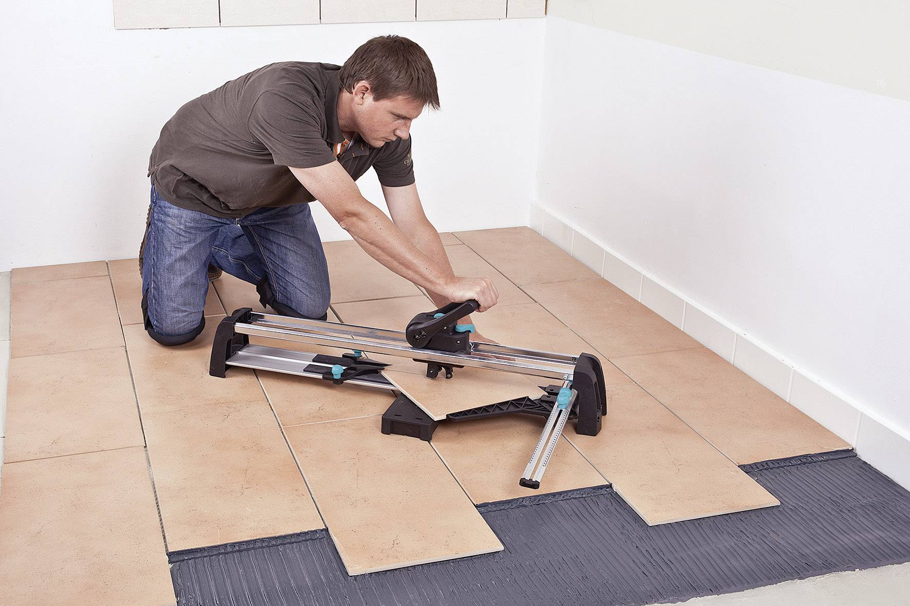 A person is kneeling on the floor, cutting several tiles with a tile cutter.