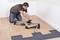 A person is kneeling on the floor, cutting several tiles with a tile cutter.