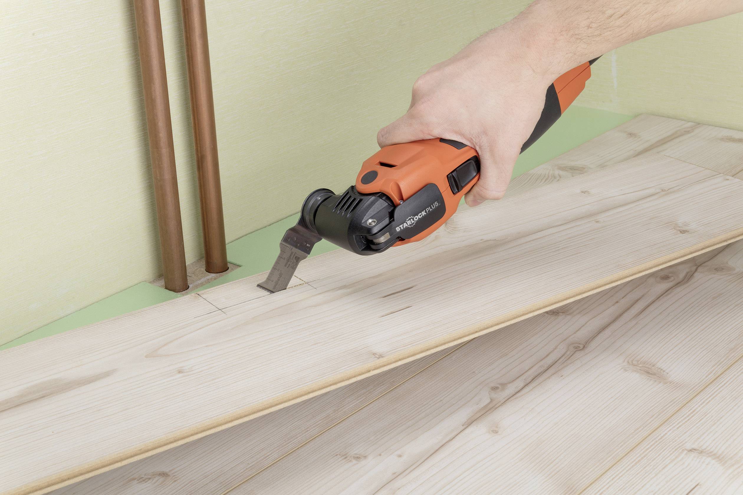 'Close-up of a hand using a multi-tool with a scraper attachment to work on laminate floor boards.'