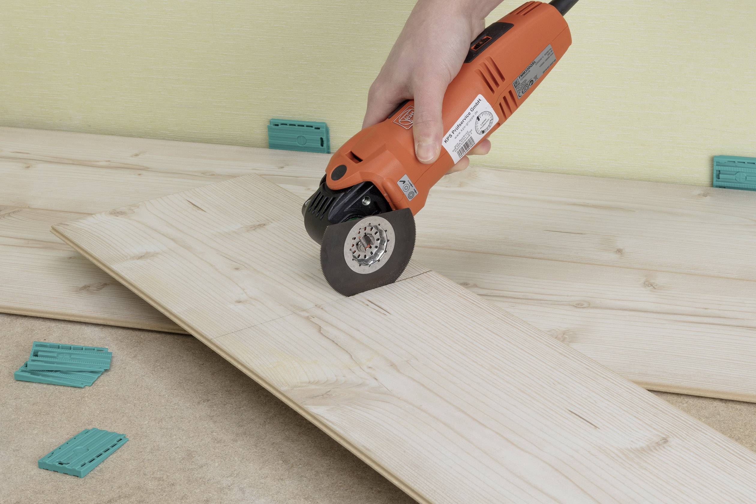 A person is cutting a wooden board with an oscillating multi-tool. Wooden planks are lying in the background.