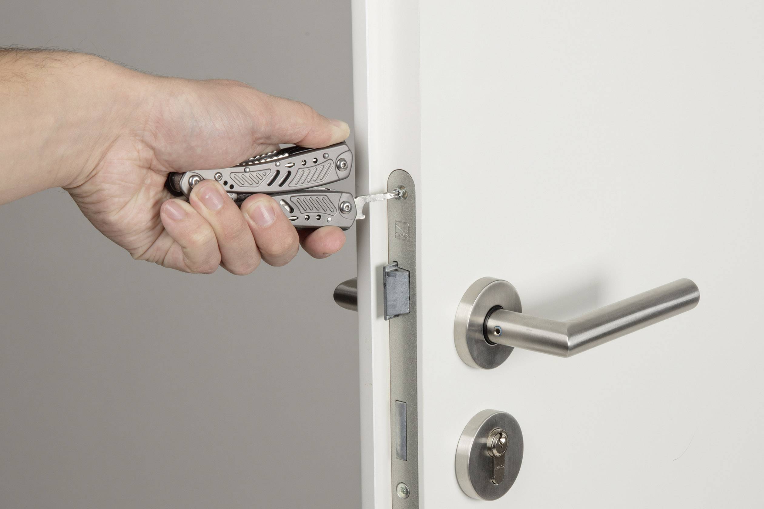 'A hand is using a multi-tool to work on a door lock.'