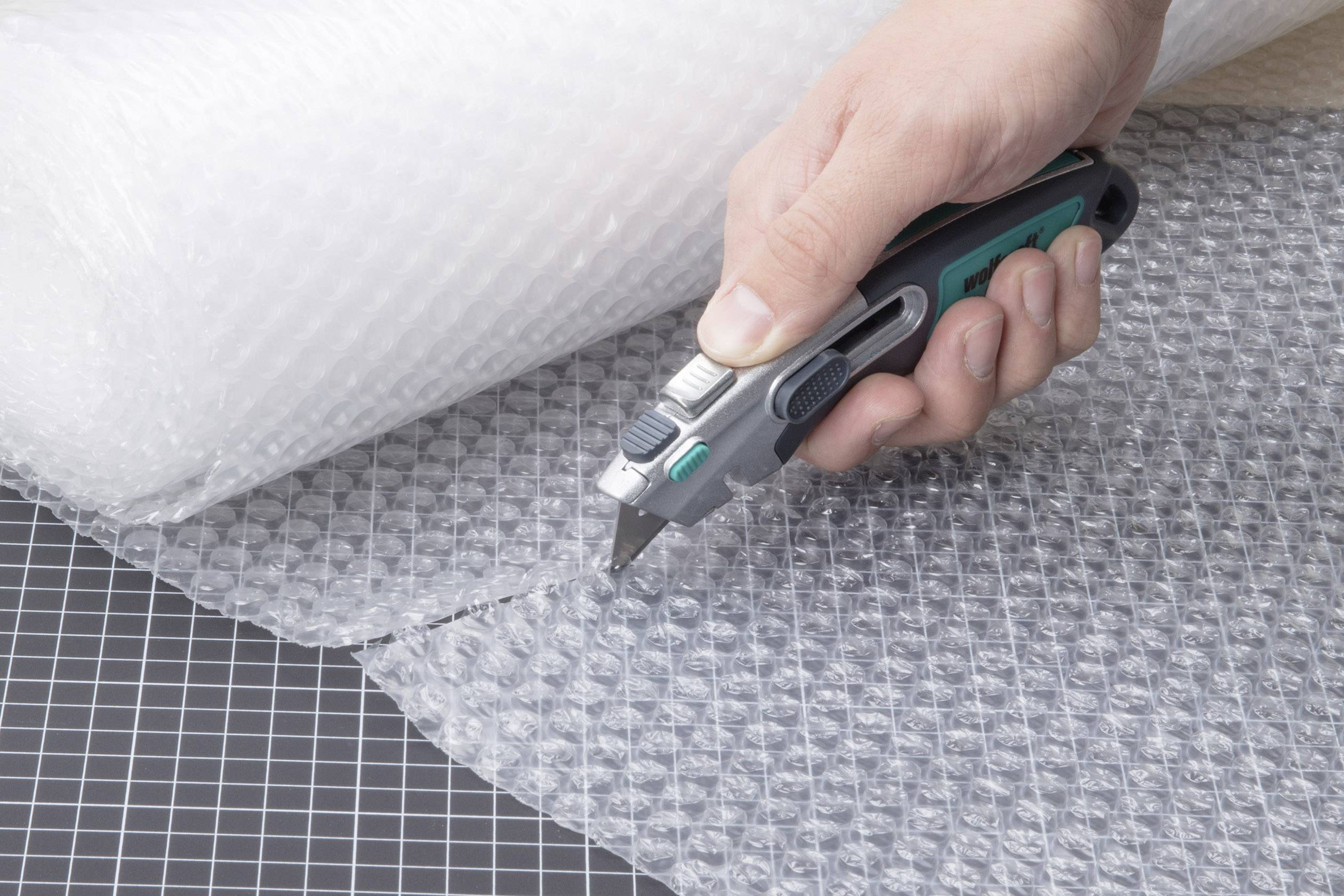 A hand is cutting bubble wrap with a craft knife on a cutting mat.