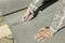 A person is cutting grey carpet with a craft knife on a wooden board. Hands and part of the tool are visible.