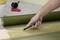 A hand is cutting a piece of mesh fabric from a roll on a workbench using a utility knife.