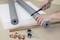 Two hands are cutting a grey pipe insulation with a craft knife; copper piping and accessories are laid out on a table.