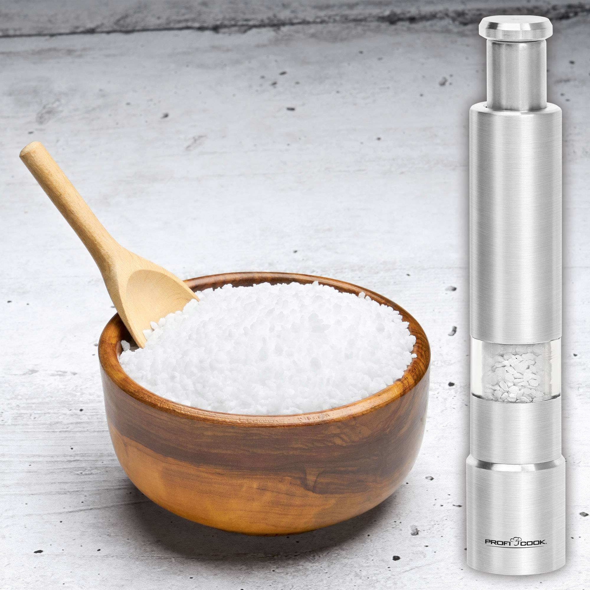 A wooden bowl filled with salt next to a silver salt and pepper mill on a grey background.
