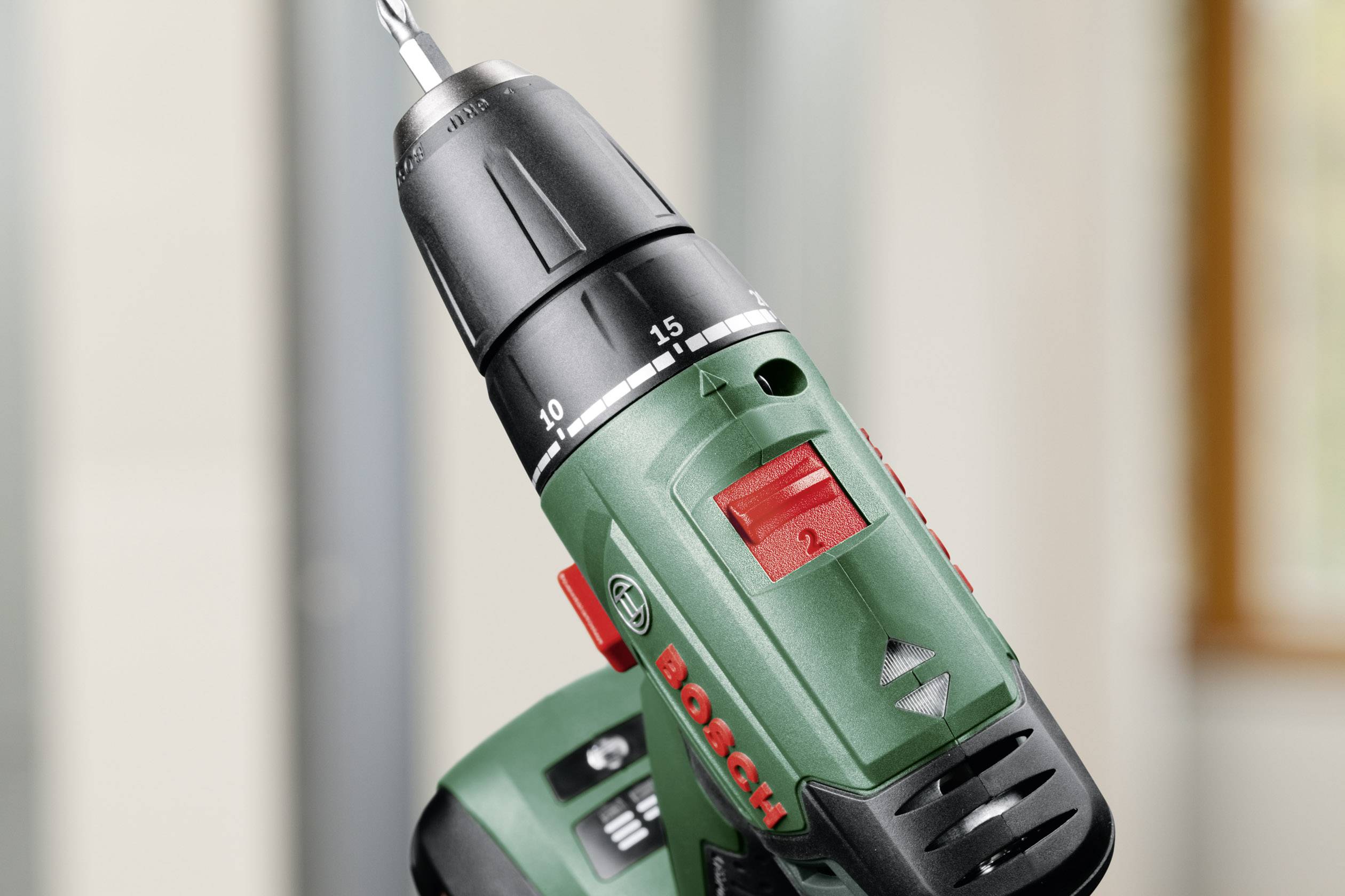 A green Bosch cordless drill with drill bit attachment, in close-up, focus on the speed and torque settings.