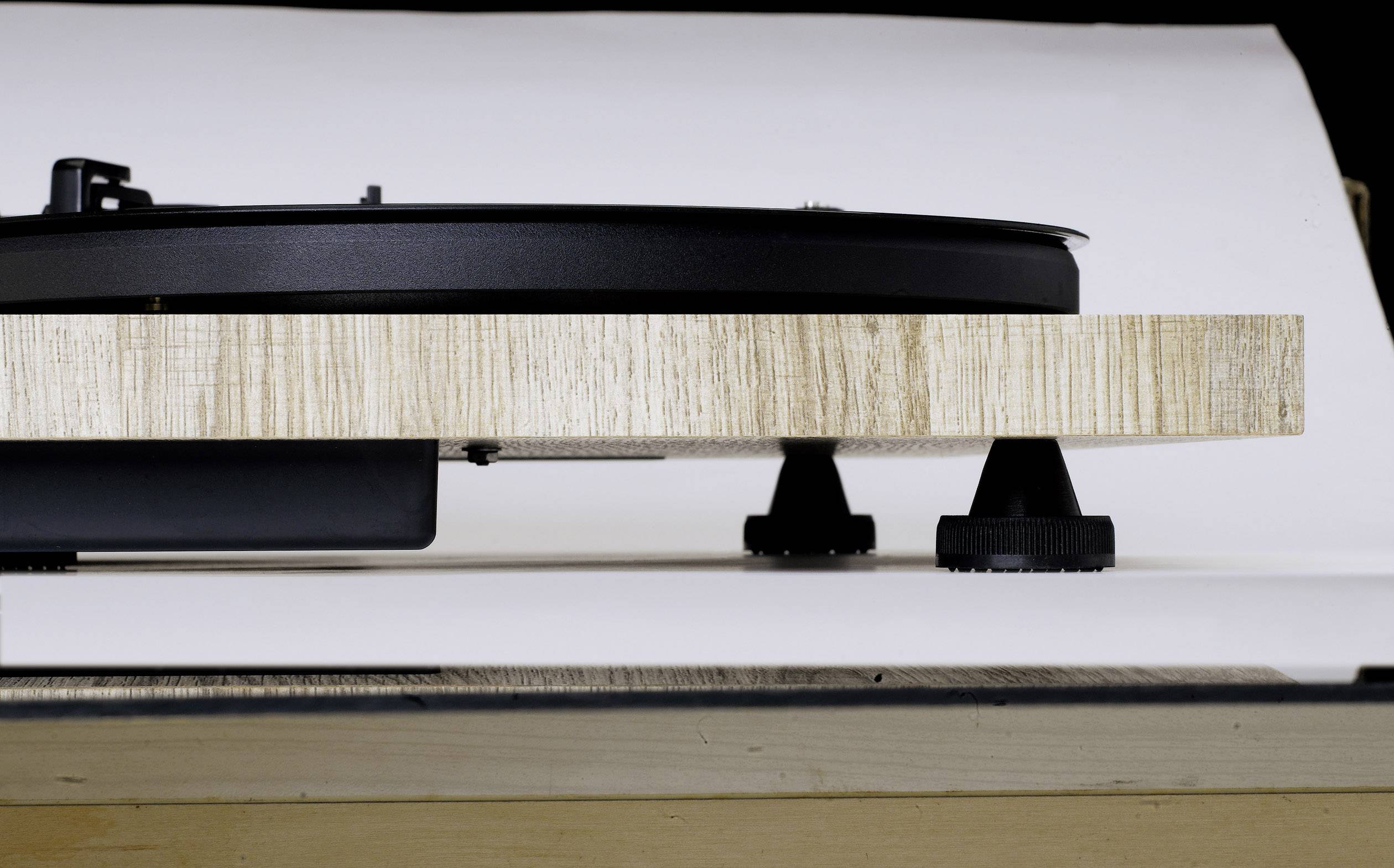 Side view of a record player with a wood-effect base and black turntable, resting on a white surface.