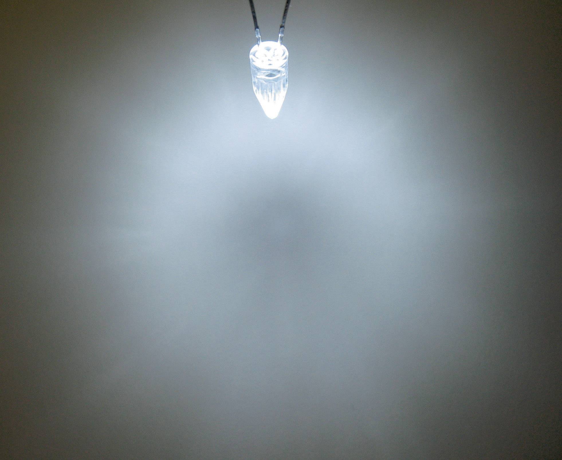 A single LED light hangs from the ceiling and shines brightly, surrounded by a soft glow in an otherwise dark room.