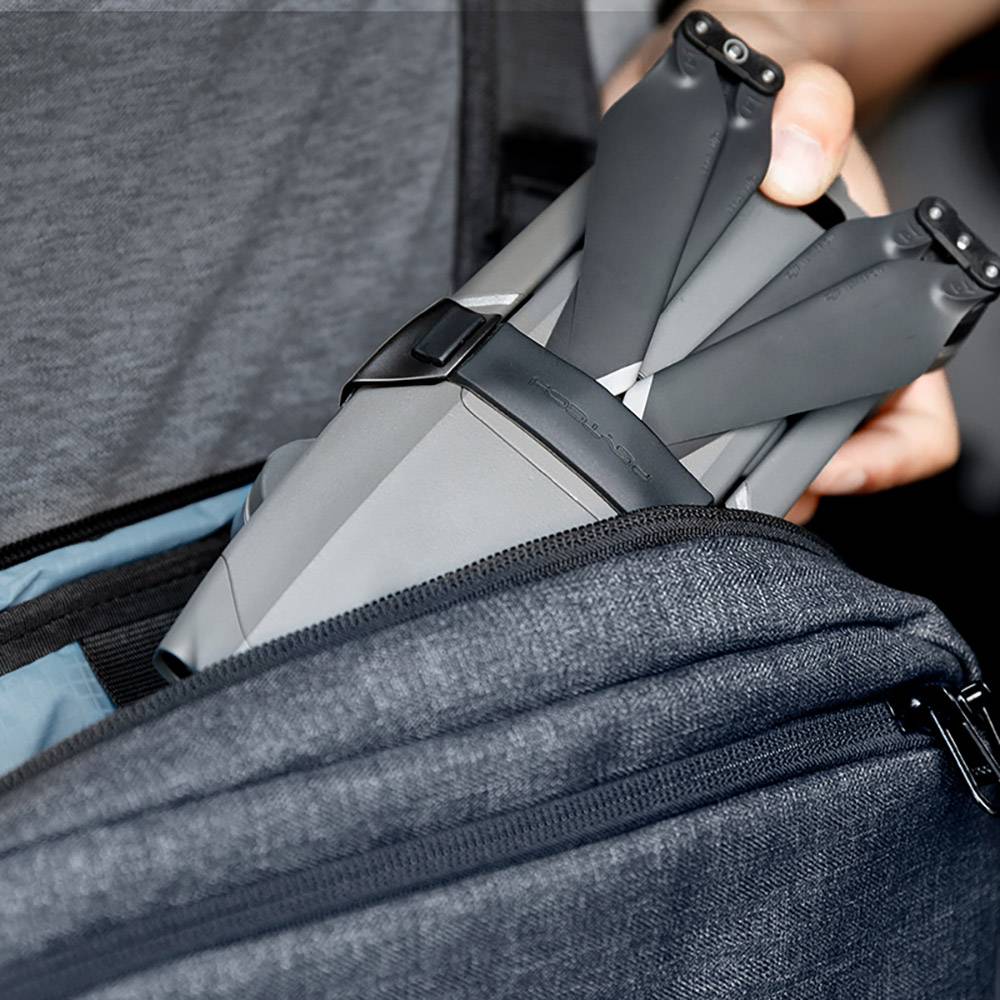 A person is removing a grey drone from a grey fabric bag. The drone has folded propellers. Background is blurred.