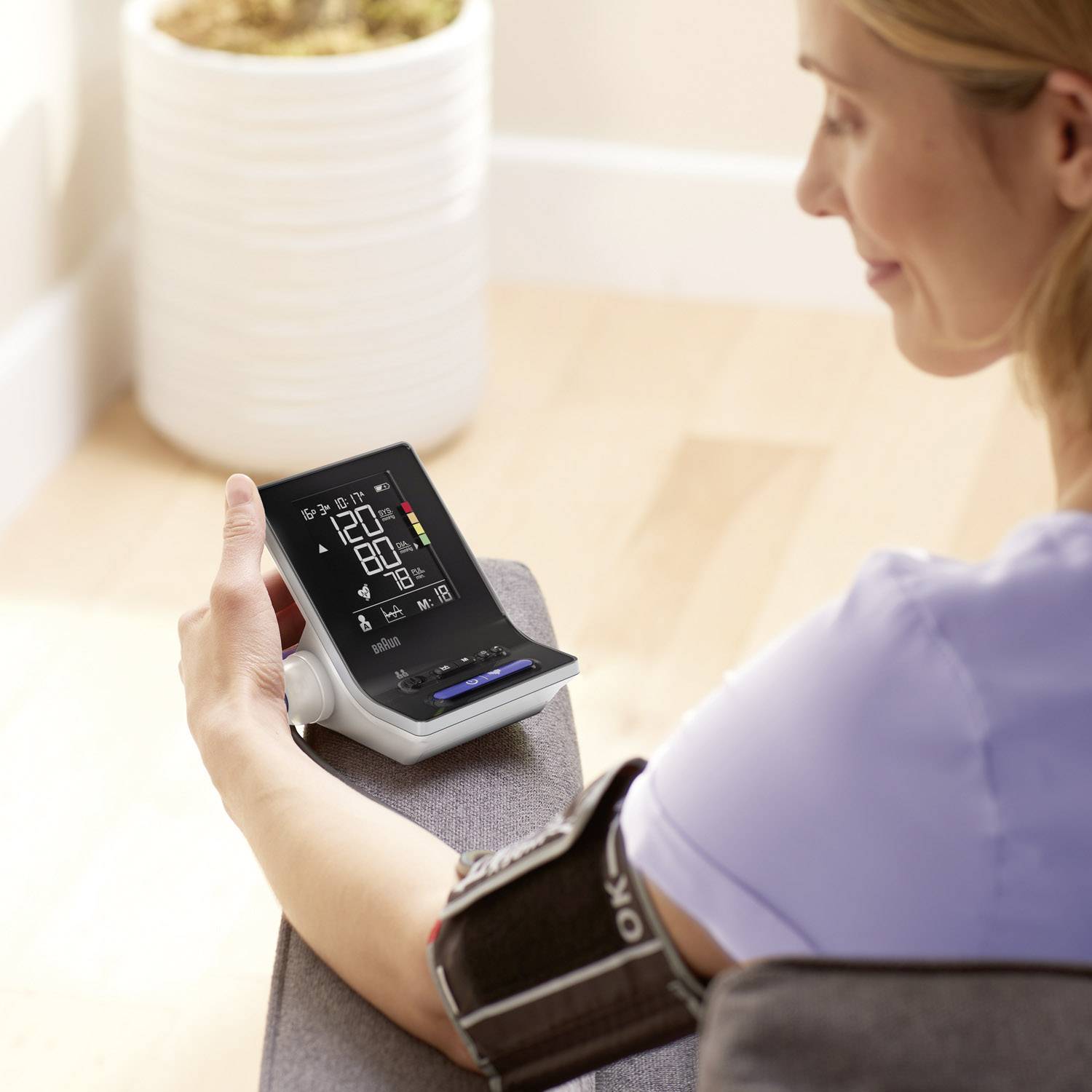 A person is measuring their blood pressure with a digital device on their arm. The display shows systolic, diastolic, and pulse rate readings.