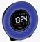 A modern alarm clock with a round, blue bezel. Digitally displays the time '13:24', day of the week 'Monday' and date '31/12'.