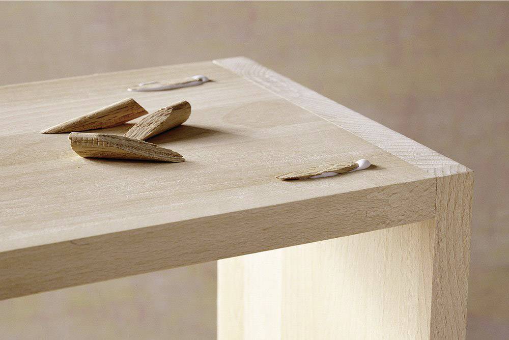 Wooden table corner with wood shavings and adhesive residue, likely from repair or assembly work.