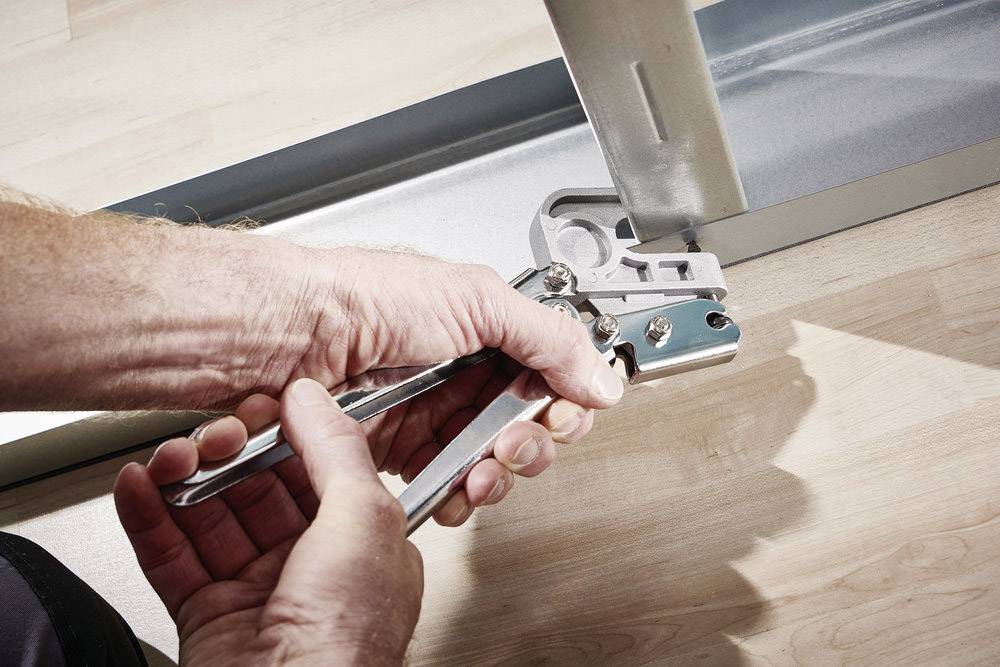 A person is using a spanner to screw a metal bracket onto a floor frame. Floor made of light-coloured wood.