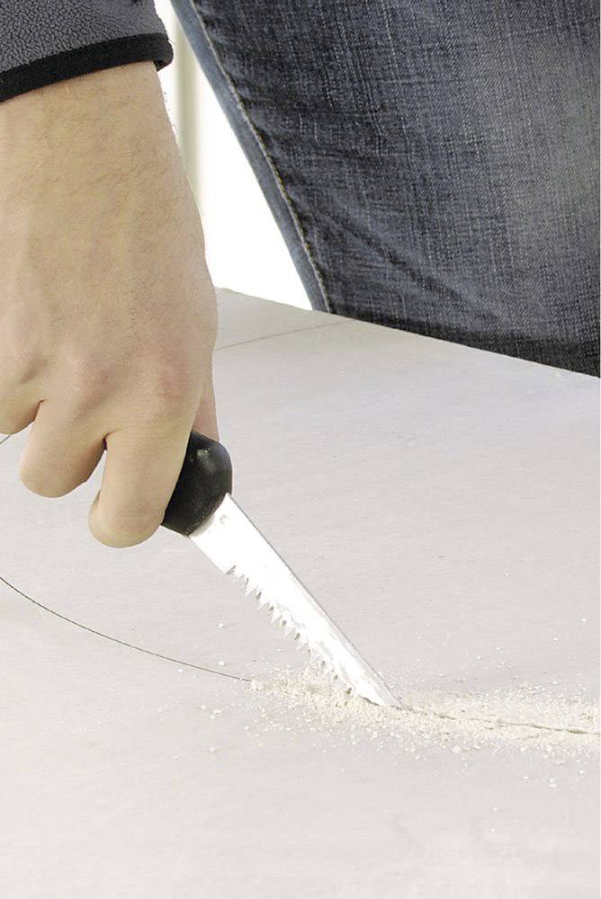 A hand is sawing through a piece of plasterboard with a fine-toothed handsaw.