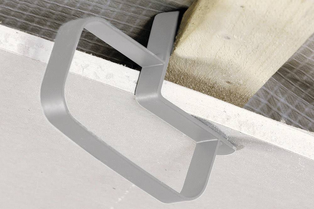 Metal mounting secures a rectangular plasterboard panel to a wooden beam. The construction is part of a ceiling installation.