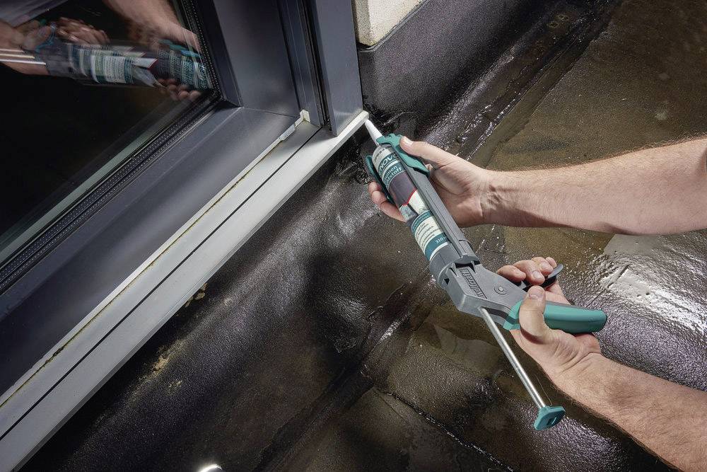 A person is sealing the window frame with a caulking gun to improve its weatherproofing and insulation.