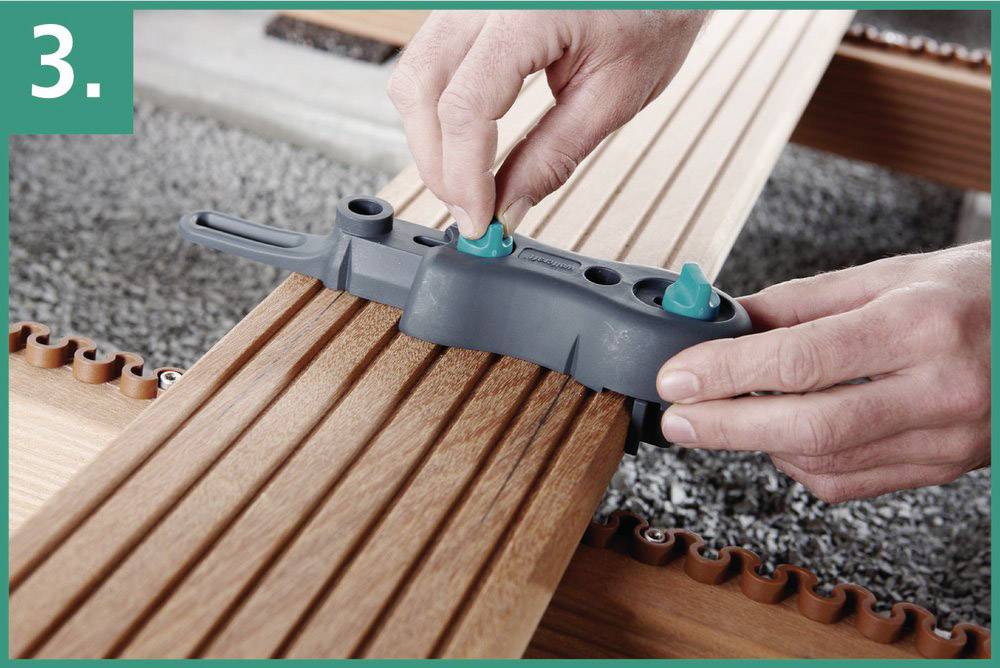 A person is using a tool to precisely align wooden boards. The tool has green buttons that are set on a wooden batten.