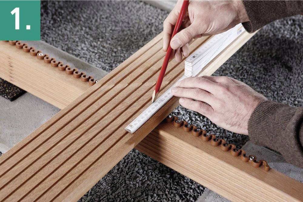 Craftwork Task: Two hands precisely measuring and marking the position on a wooden batten using a red pencil and a measuring tape.