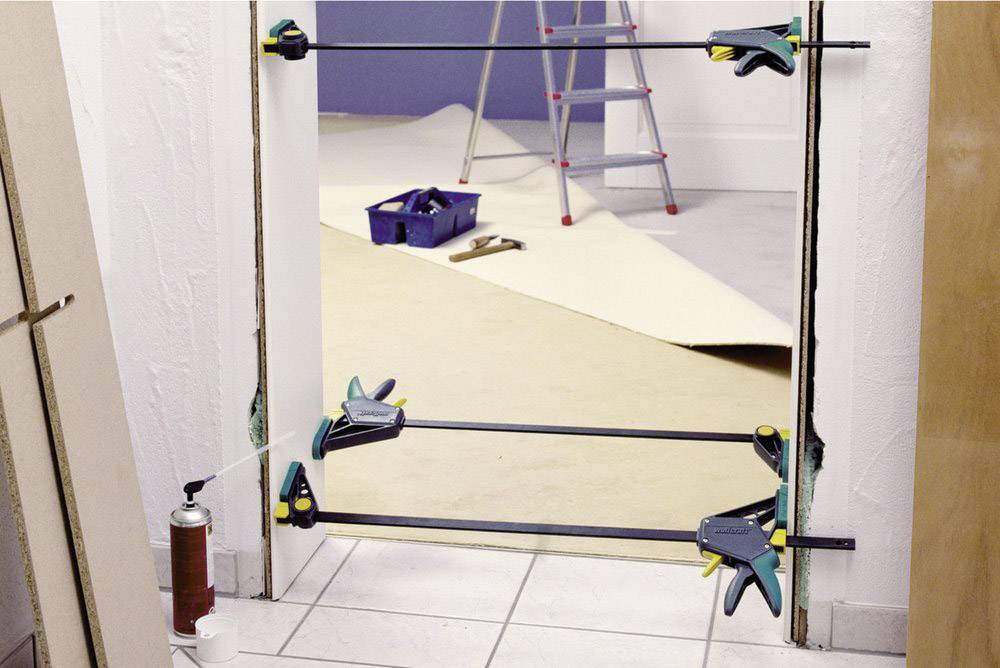 Door frame is installed using tensioning tools; background shows ladder and painting equipment, suggesting renovation work.
