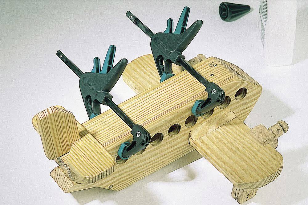 Wooden toy aeroplane under construction, secured with two clamps; depicting a stage of the craftsman's building process.