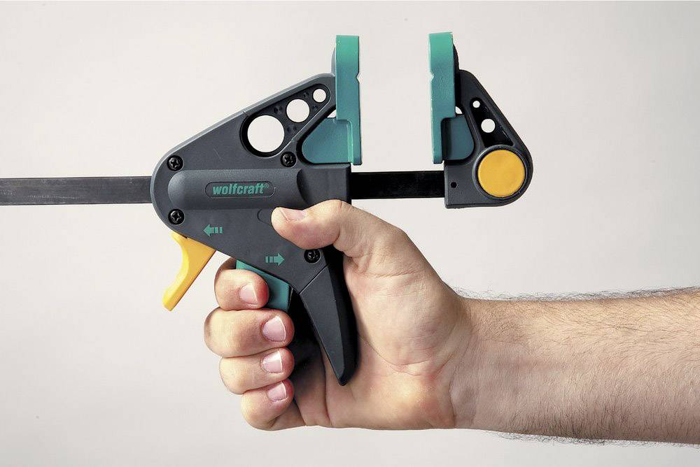 A hand is holding a clamp with a handle in black and green accents. The clamp is partially opened.