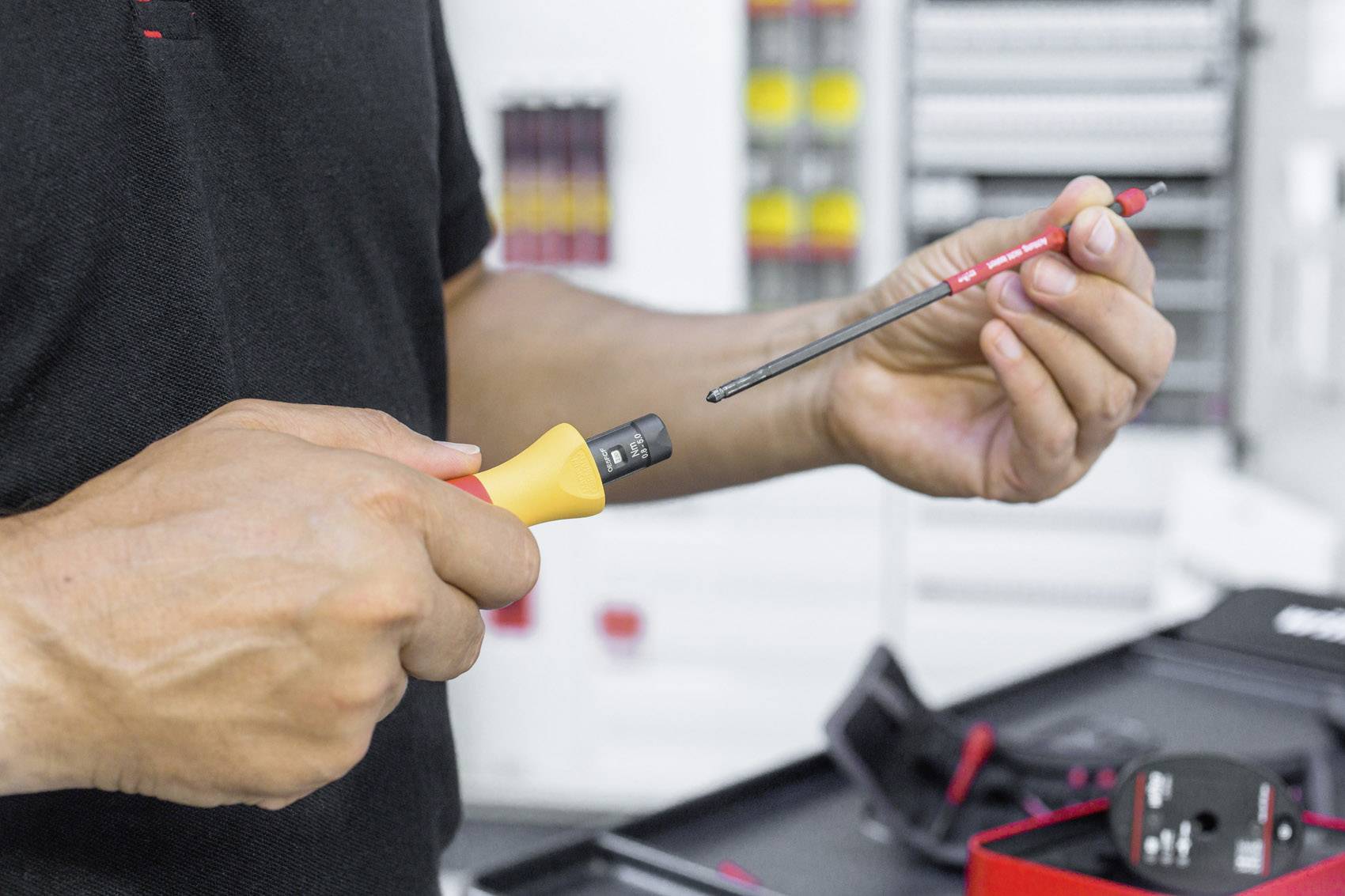 A person is holding a screwdriver and a switched-on electrical testing device in a workshop.