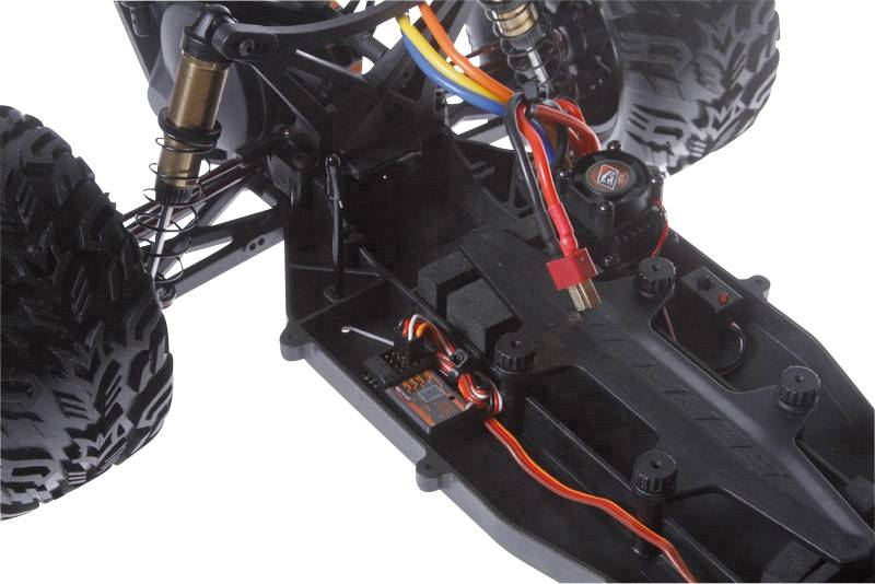 Close-up of a model car chassis with visible cables, shock absorbers, and tyres. The focus is on the technical detailed view.