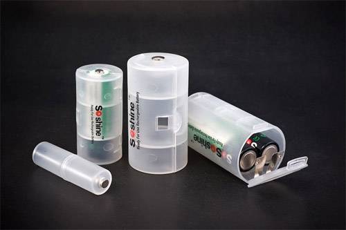 Three transparent plastic boxes, each containing batteries of varying sizes, on a dark background. The boxes are partially open.