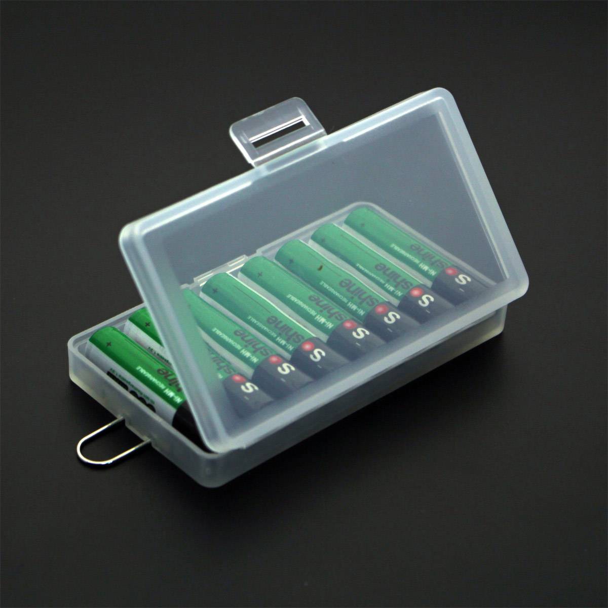 A transparent box, open, contains several green AA batteries, neatly arranged. It is situated on a dark background.