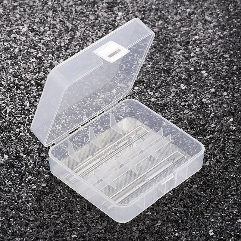 A transparent empty plastic box with compartments, slightly open, rests on a grainy, black surface.