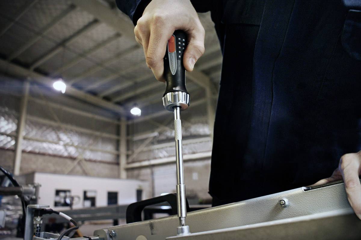 A person is assembling a metal construction with a screwdriver in a workshop.