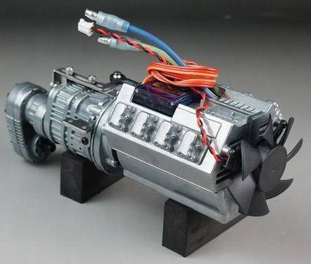 A metallic engine with multiple cables on top and fan blades at the front, mounted on black stands, against a grey background.