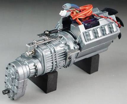 A silver miniature motor with visible gears and red cables, displayed on black blocks, against a grey background.