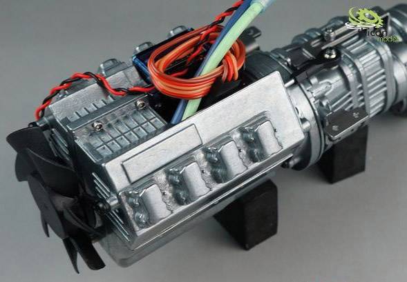 Close-up of a model engine with visible cables and metal parts, positioned on a grey background.