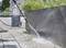 A person is cleaning paving stones with a pressure washer. Plants and a cleaning device are visible in the background.