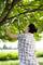 A woman is cutting branches with pruning shears from a tree. The background shows a meadow and trees in sunny weather.