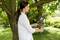 A person is pruning branches from a tree using garden shears. The surroundings are a green garden with bright daylight.