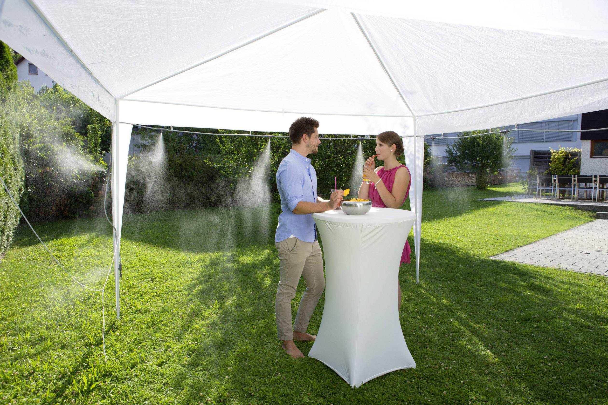 A man and a woman are standing under a white pavilion in a garden, drinking refreshments and chatting.